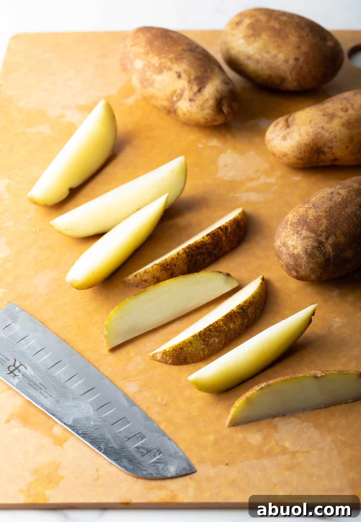 Raw potato wedges sitting on a cutting board next to a knife.
