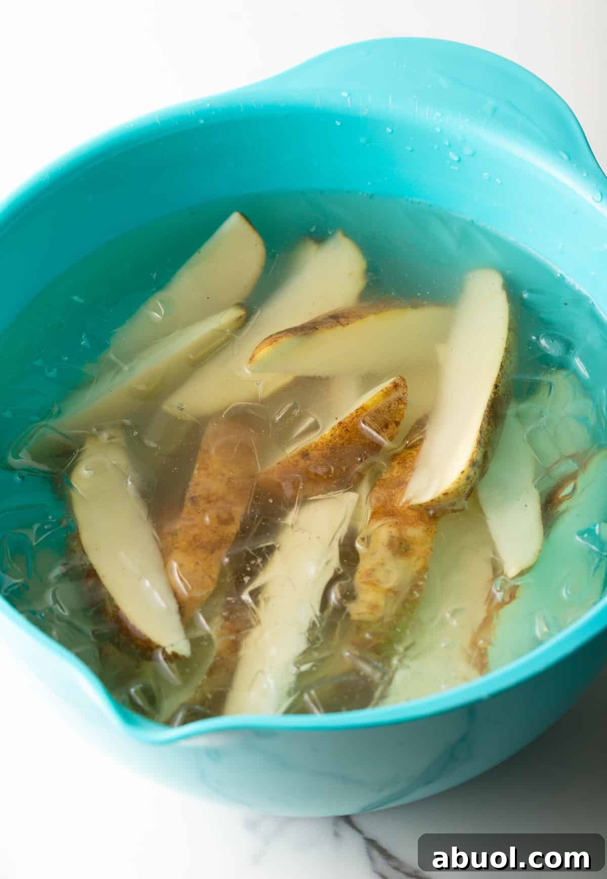 Raw potato wedges sitting in an ice bath in a blue bowl.