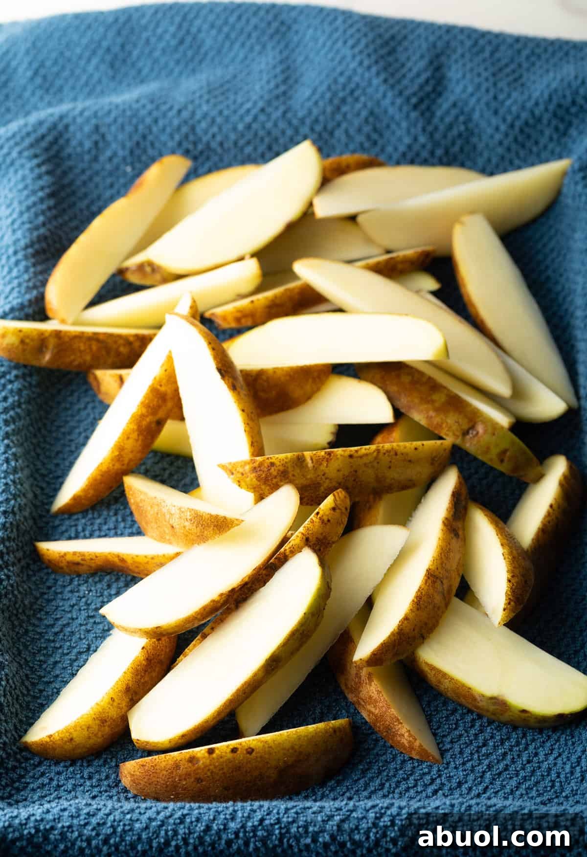 Raw potato wedges are draining on a towel to remove excess moisture.