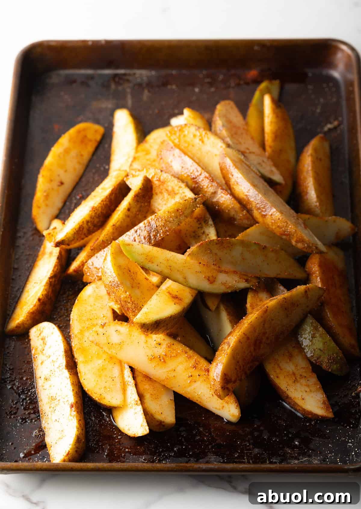 Potato wedges that have been drizzled with olive oil and seasoned, sitting on a baking sheet.