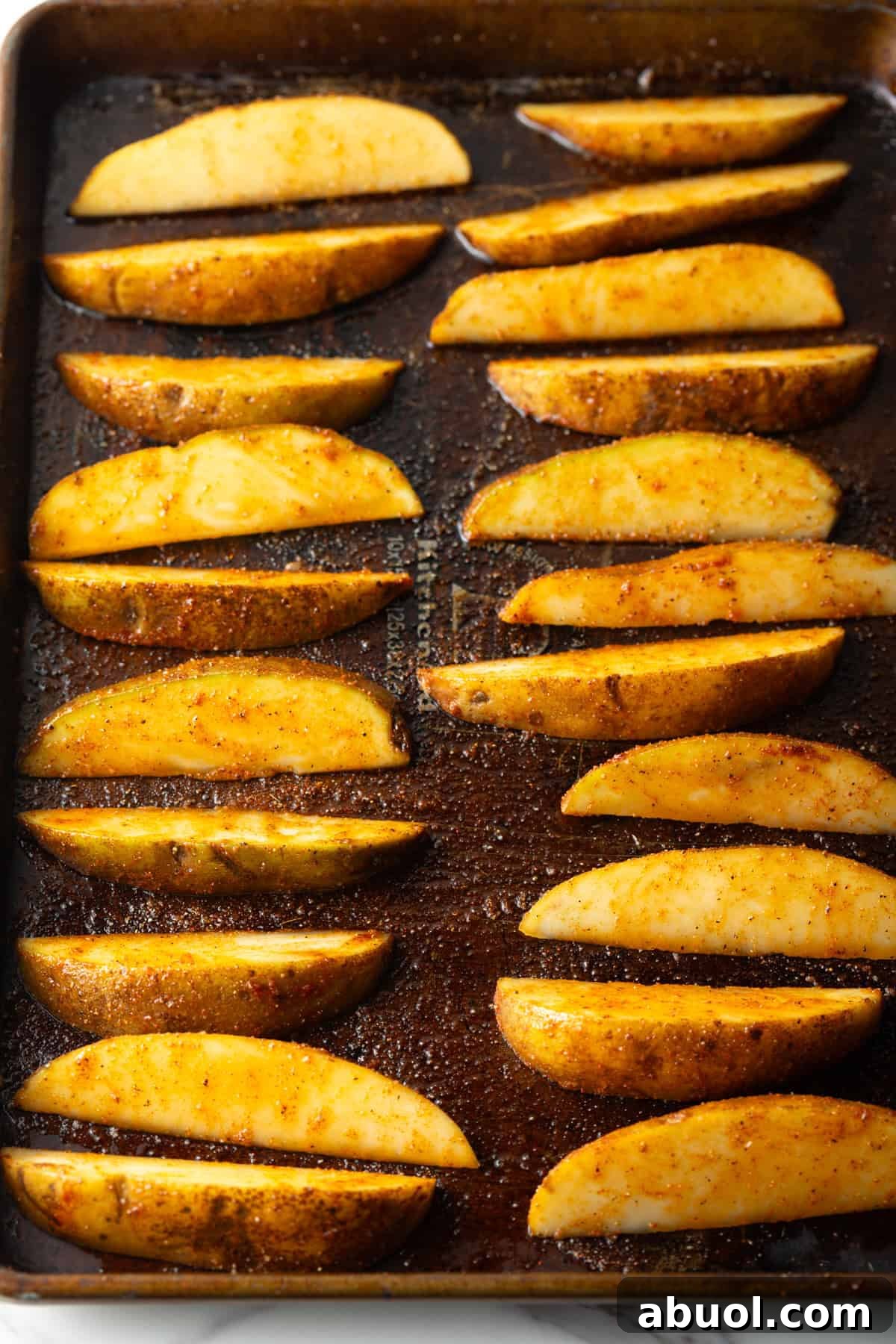 Homemade potato wedges arranged on a baking sheet, ready for baking.