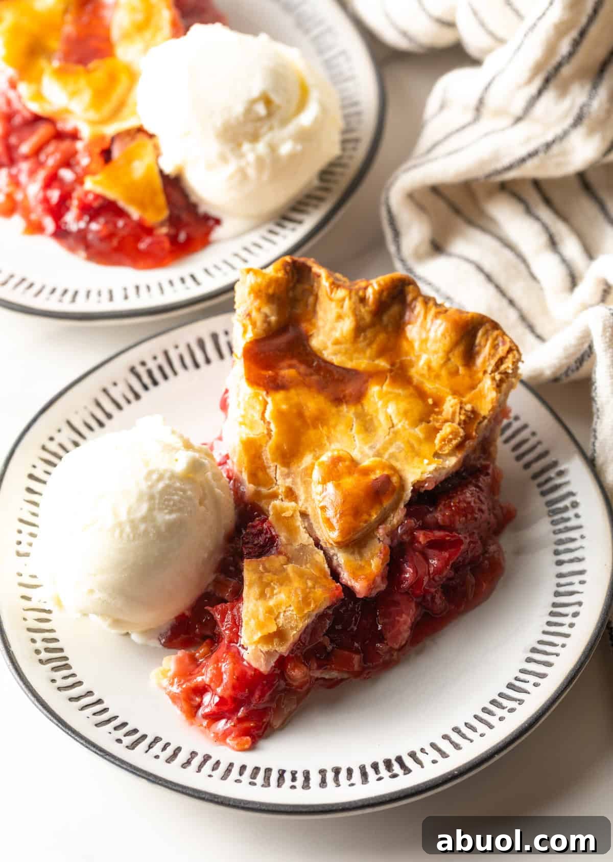 A slice of strawberry rhubarb pie sitting on a white plate, with a scoop of vanilla ice cream on the side.