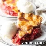 A slice of strawberry rhubarb pie with a scoop of vanilla ice cream on the side.