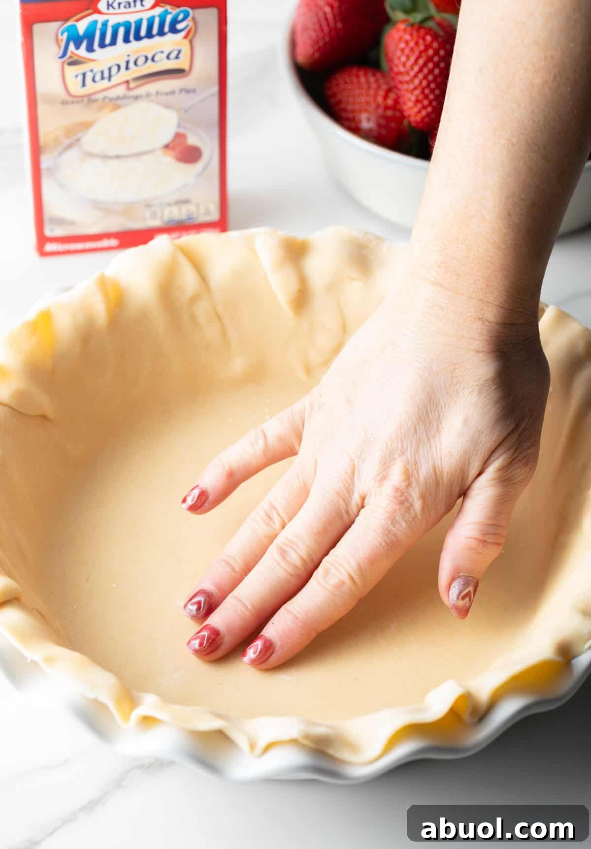 A hand is pressing a pie dough crust into a pie plate.
