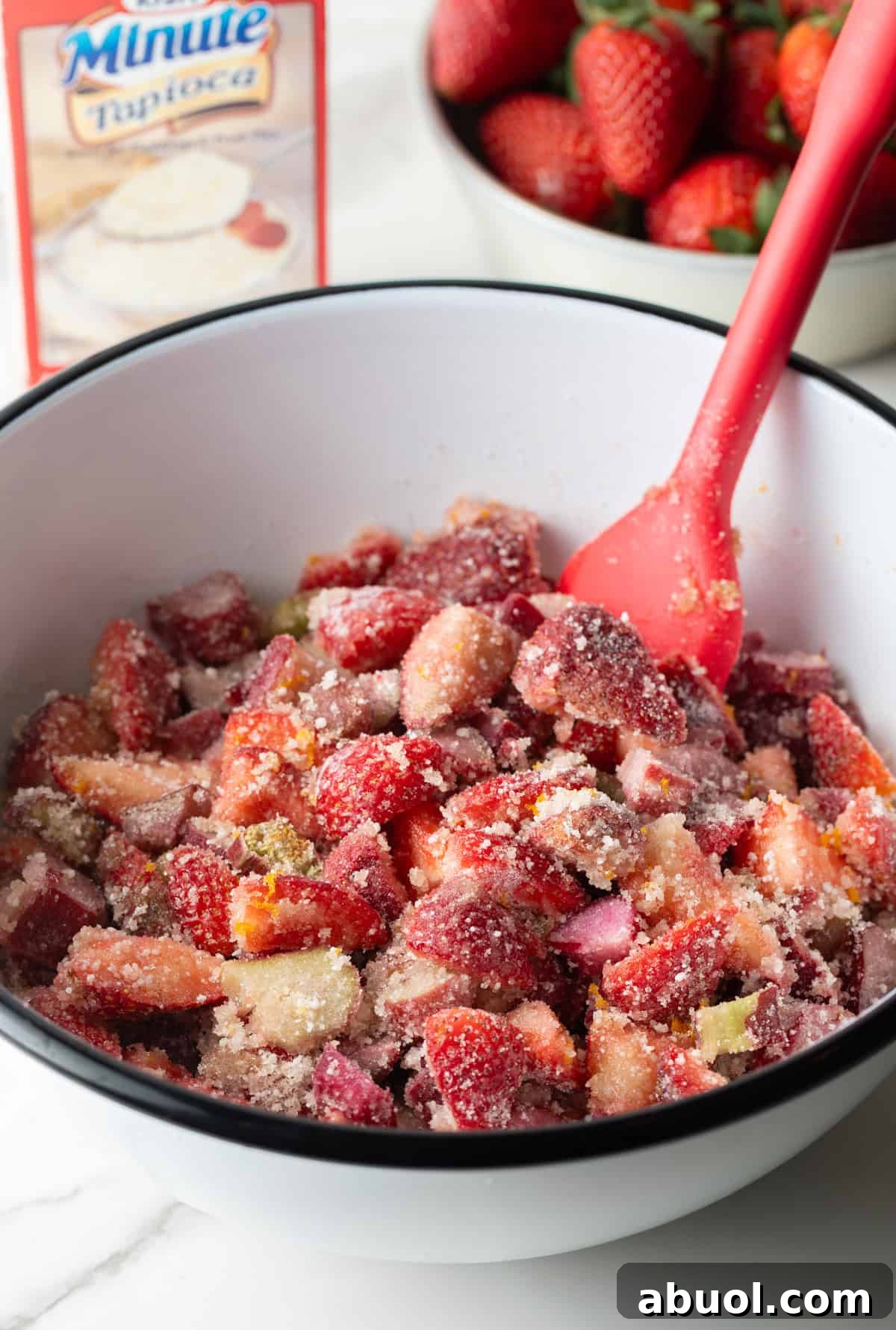 A strawberry rhubarb pie mixture is being stirred in a mixing bowl.