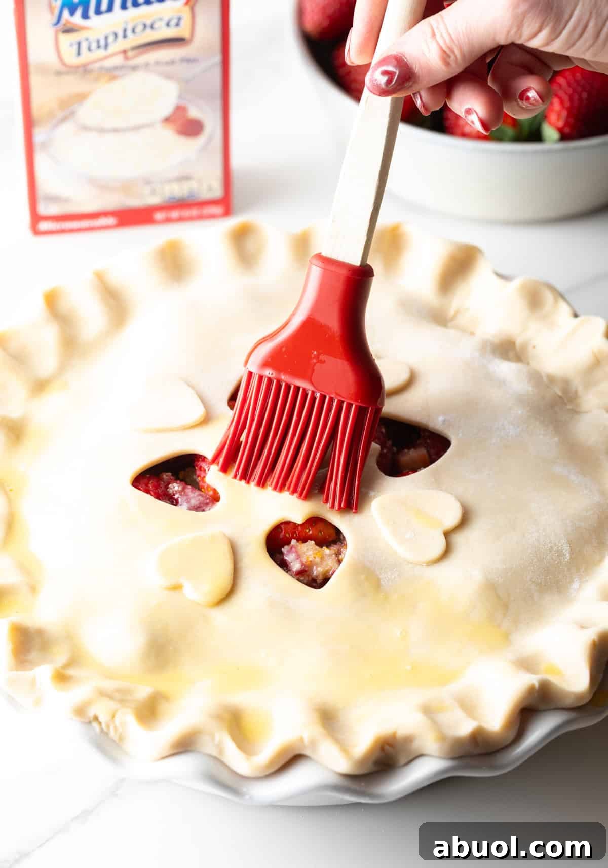 An egg wash is being brushed onto the top of a rhubarb strawberry pie.