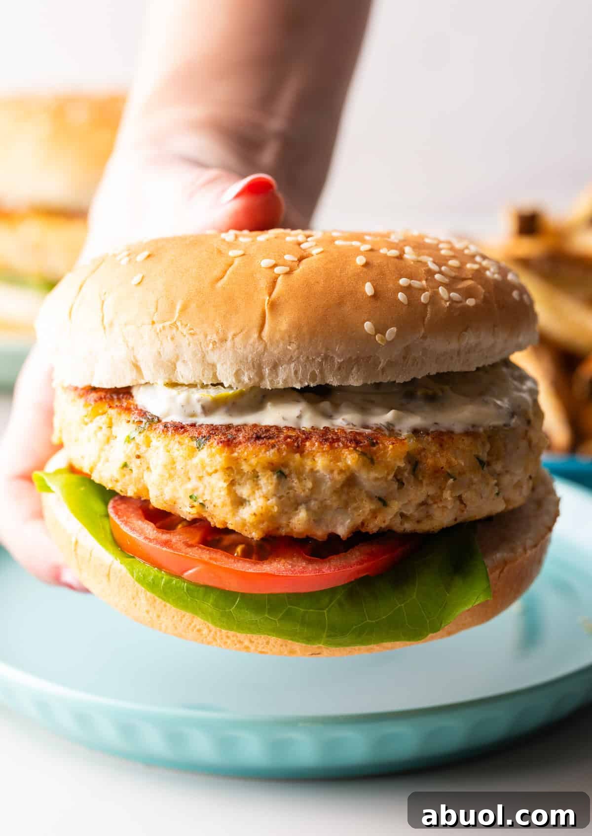 A hand is holding a fish hamburger above a blue plate.