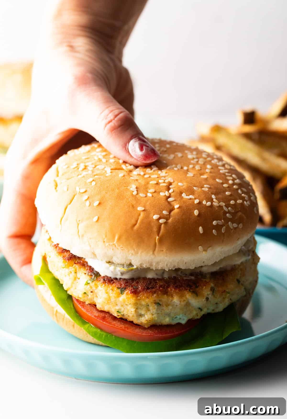 A hand is holding a fish patty hamburger above a blue plate.