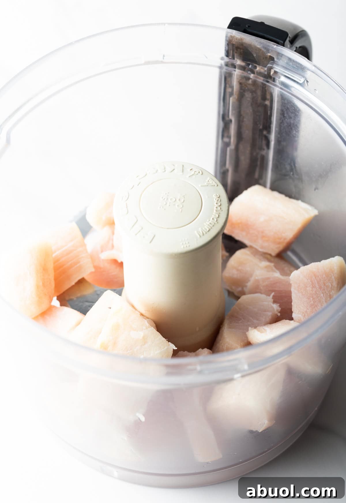 Chunks of raw white fish are sitting in a food processor for a fish burger recipe.