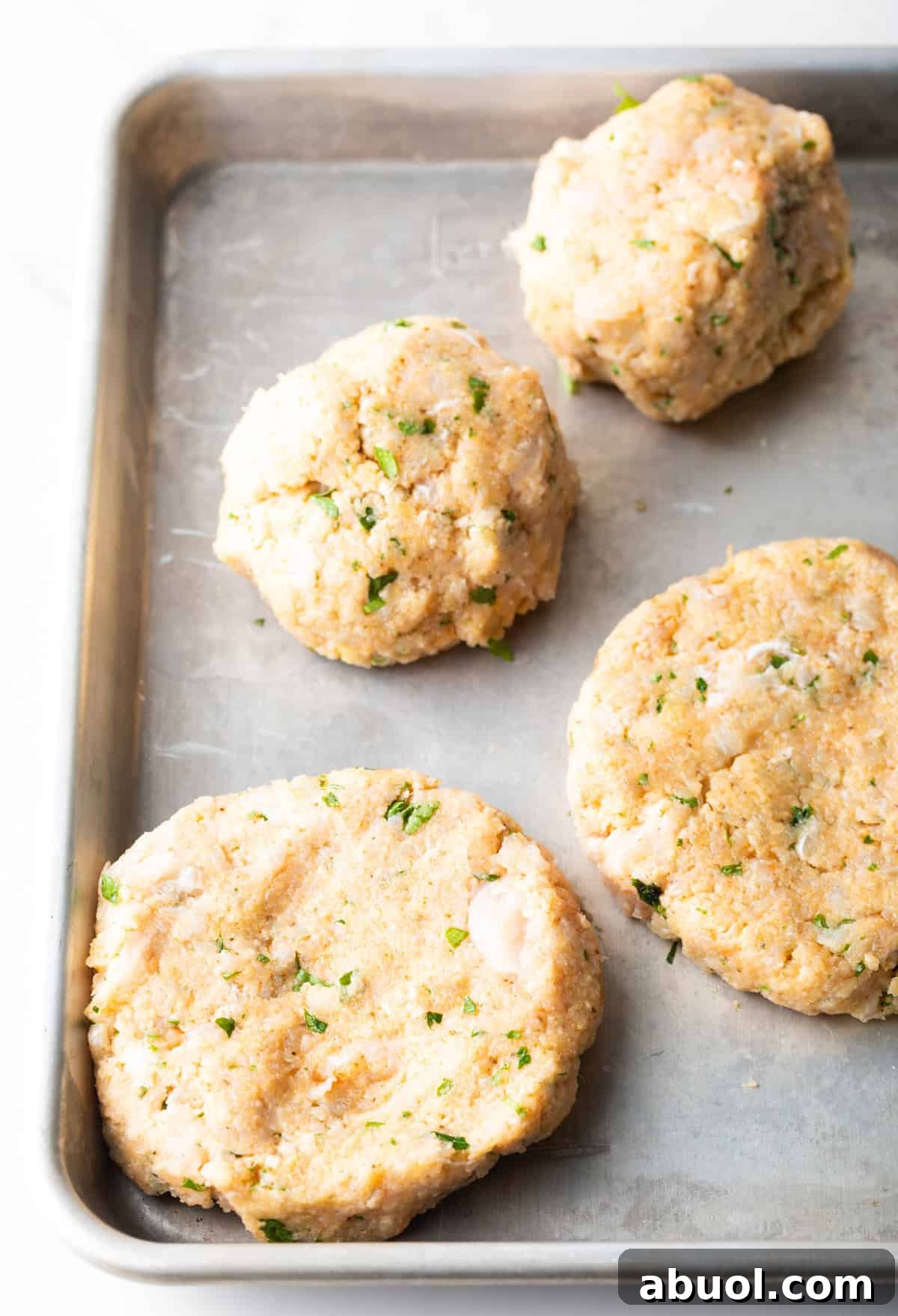 Fish burger patties are sitting on a parchment-lined baking sheet.