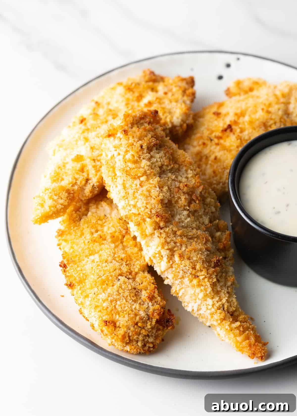 A plate of crispy air fryer chicken tenders next to a ramekin of white sauce.