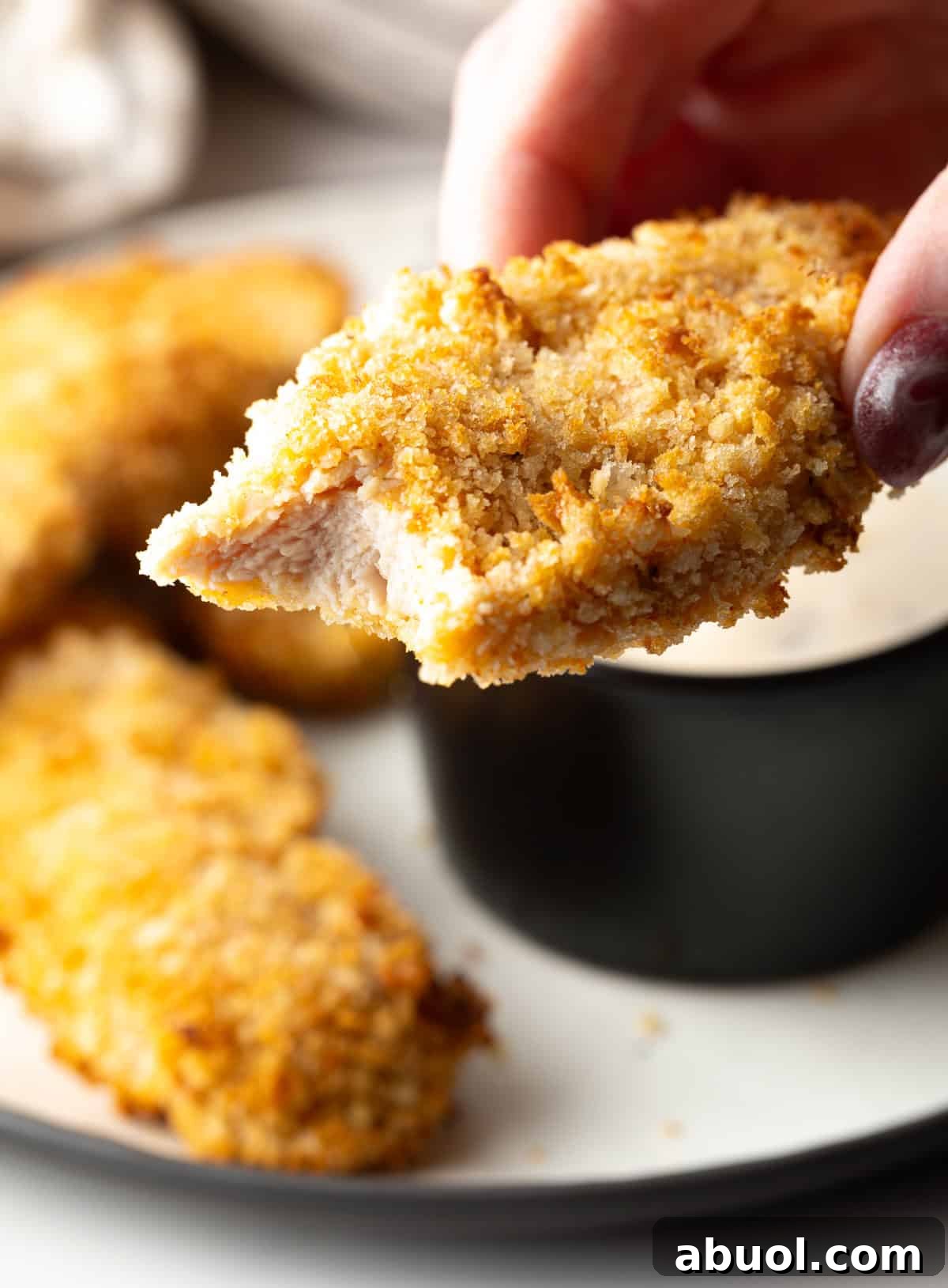 A hand is holding a crispy air fried chicken tender with a bite taken out.