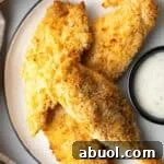 A plate of crispy air fried chicken tenders next to a ramekin of white sauce.