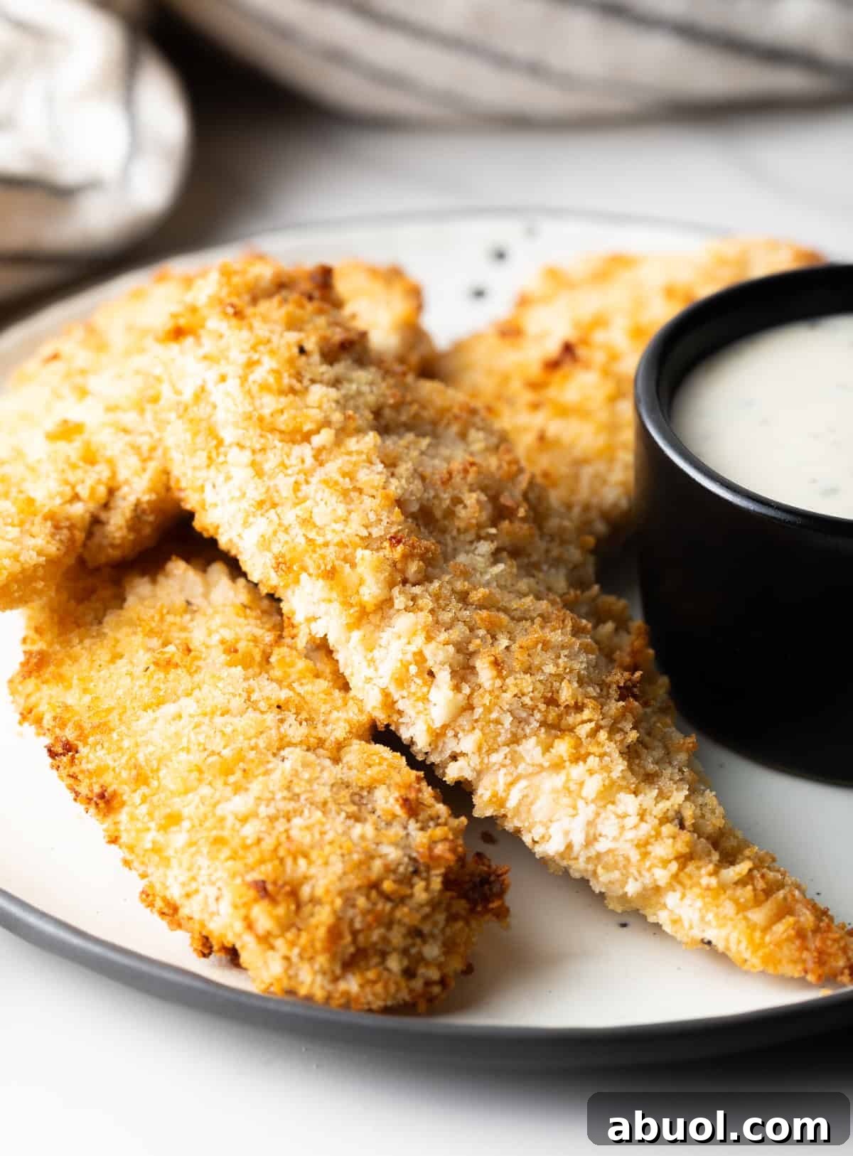 A side view of a white plate filled with crispy air fryer chicken tenders with a ramekin of dipping sauce on the side.