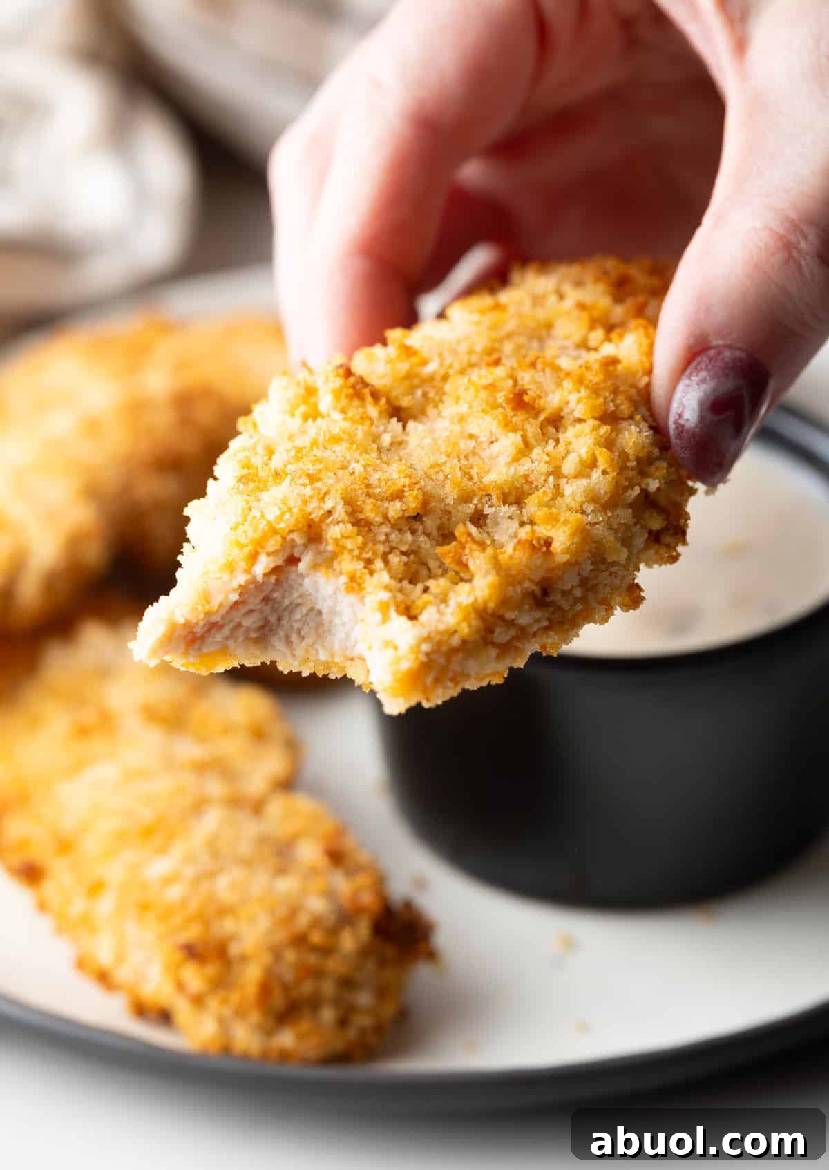 A hand is holding a chicken tender made in the air fryer with a bite taken out.