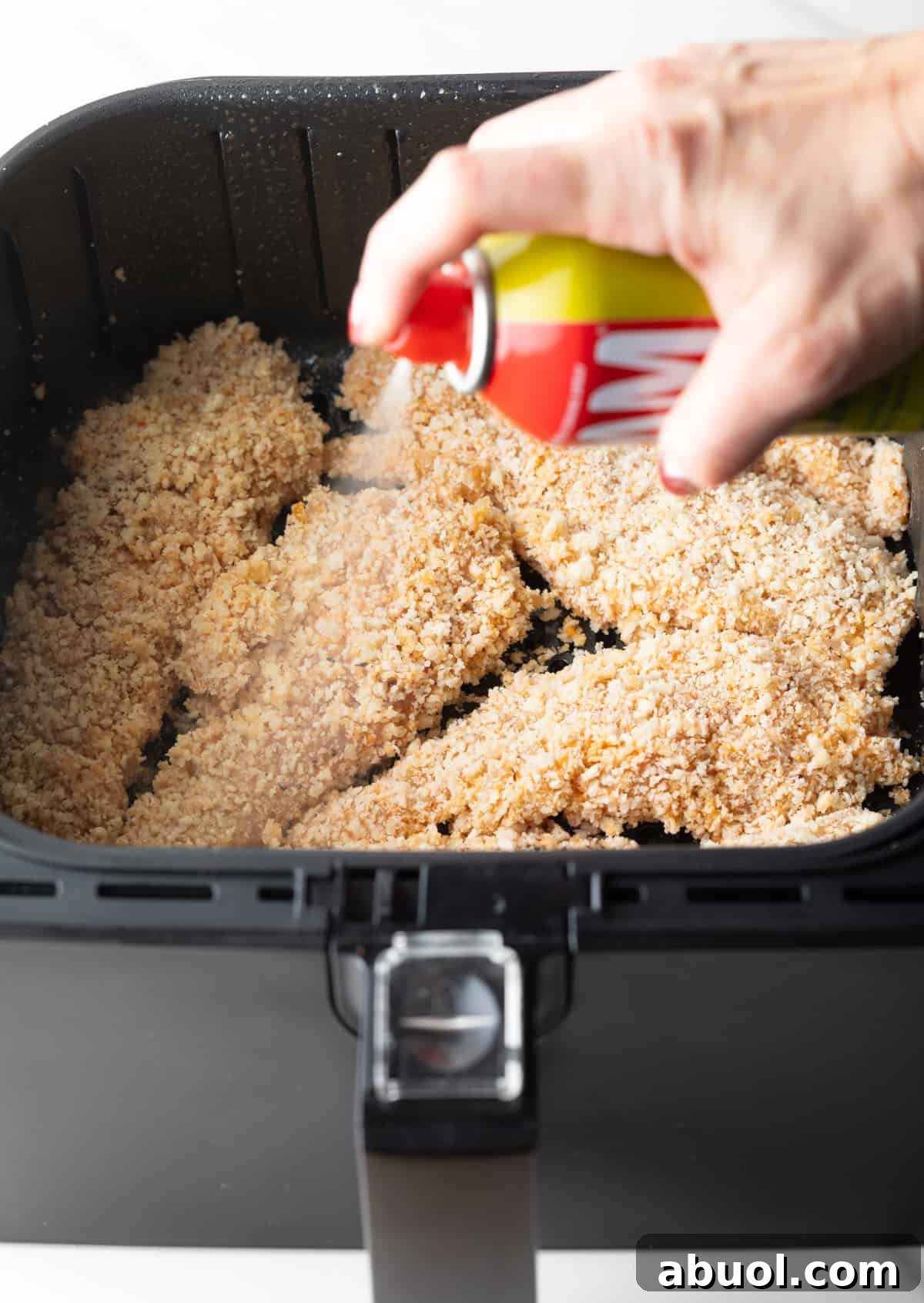 Chicken tenders in the air fryer that are being sprayed with cooking oil.