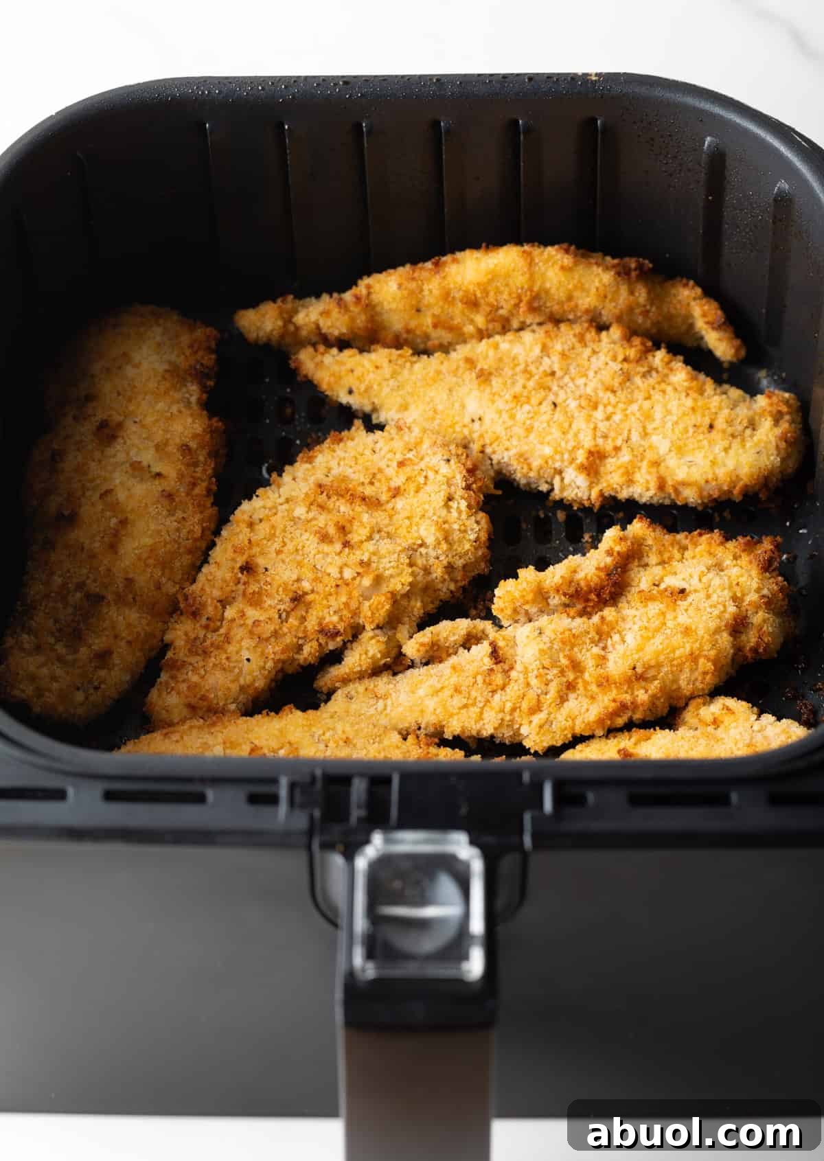 Crispy and golden air fried chicken tenders sitting in an air fryer basket.