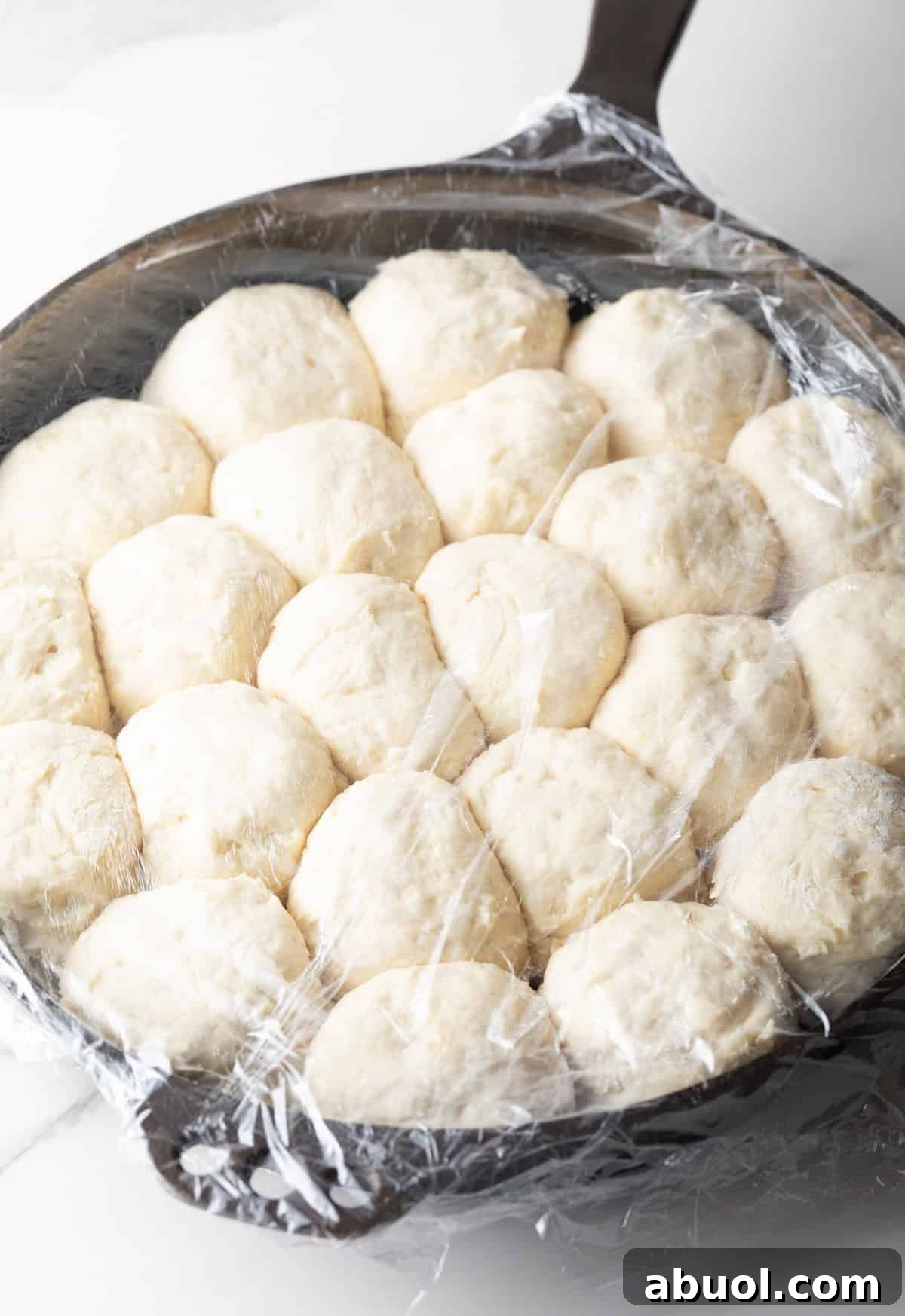 Risen angel biscuits in a skillet covered in plastic wrap.