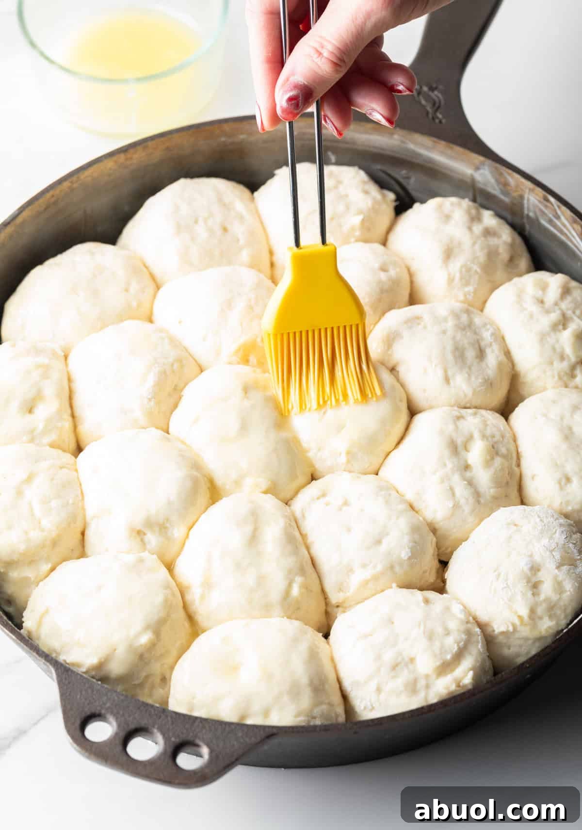Angel biscuit dough is being brushed with butter, ready for baking.