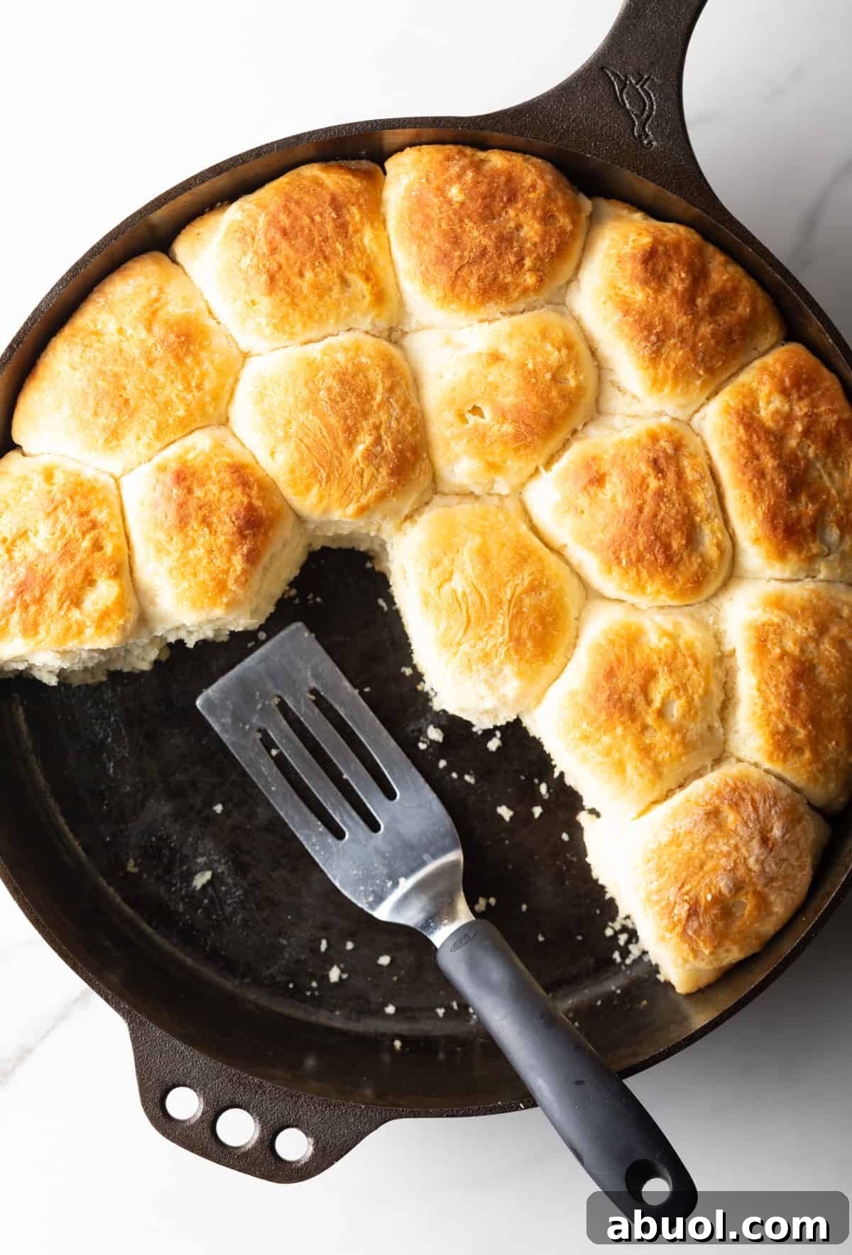 An overhead shot of a black skillet filled with an old-fashioned yeast biscuits recipe, with a metal spatula ready for serving.