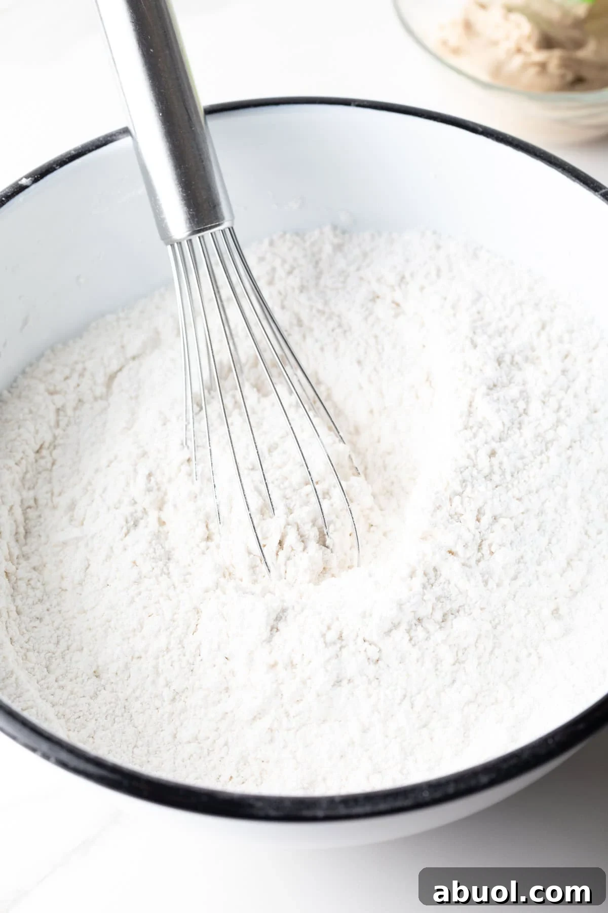 A flour mixture for an angel biscuits recipe is being whisked in a white bowl.