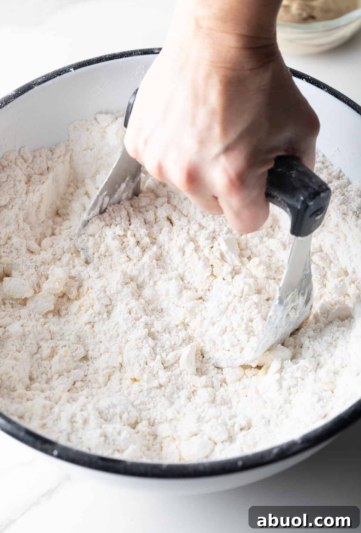 A hand holding a pastry cutter that is mixing butter and shortening into an angel biscuit mix.