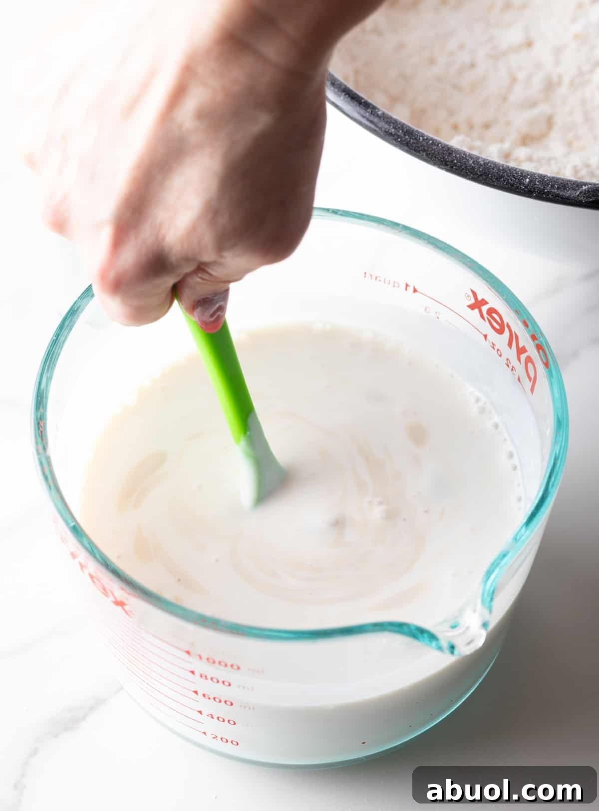 A bloomed yeast mixture is being stirred into a measuring bowl full of buttermilk.