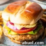 A ground chicken burger topped with condiments and vegetables between two hamburger buns.