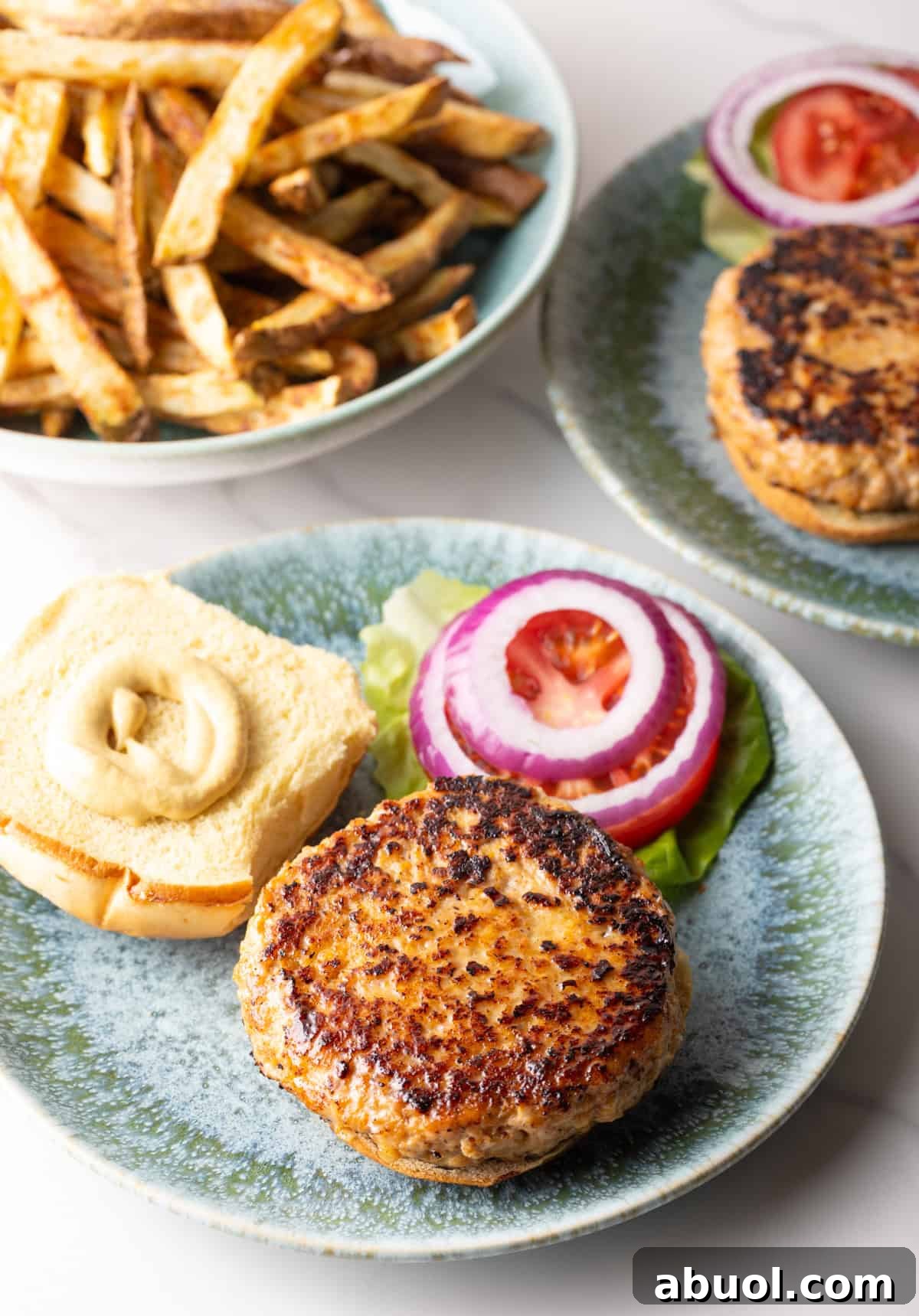 An open chicken patty sandwich with mayonnaise on half of the bun, sitting next to lettuce, tomatoes, and red onions.