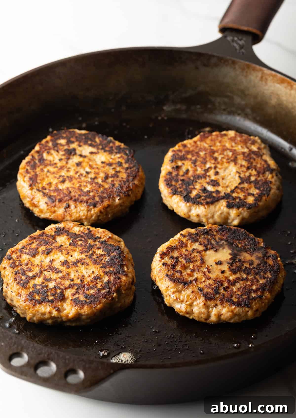 Four ground chicken burgers are being cooked in a black skillet.
