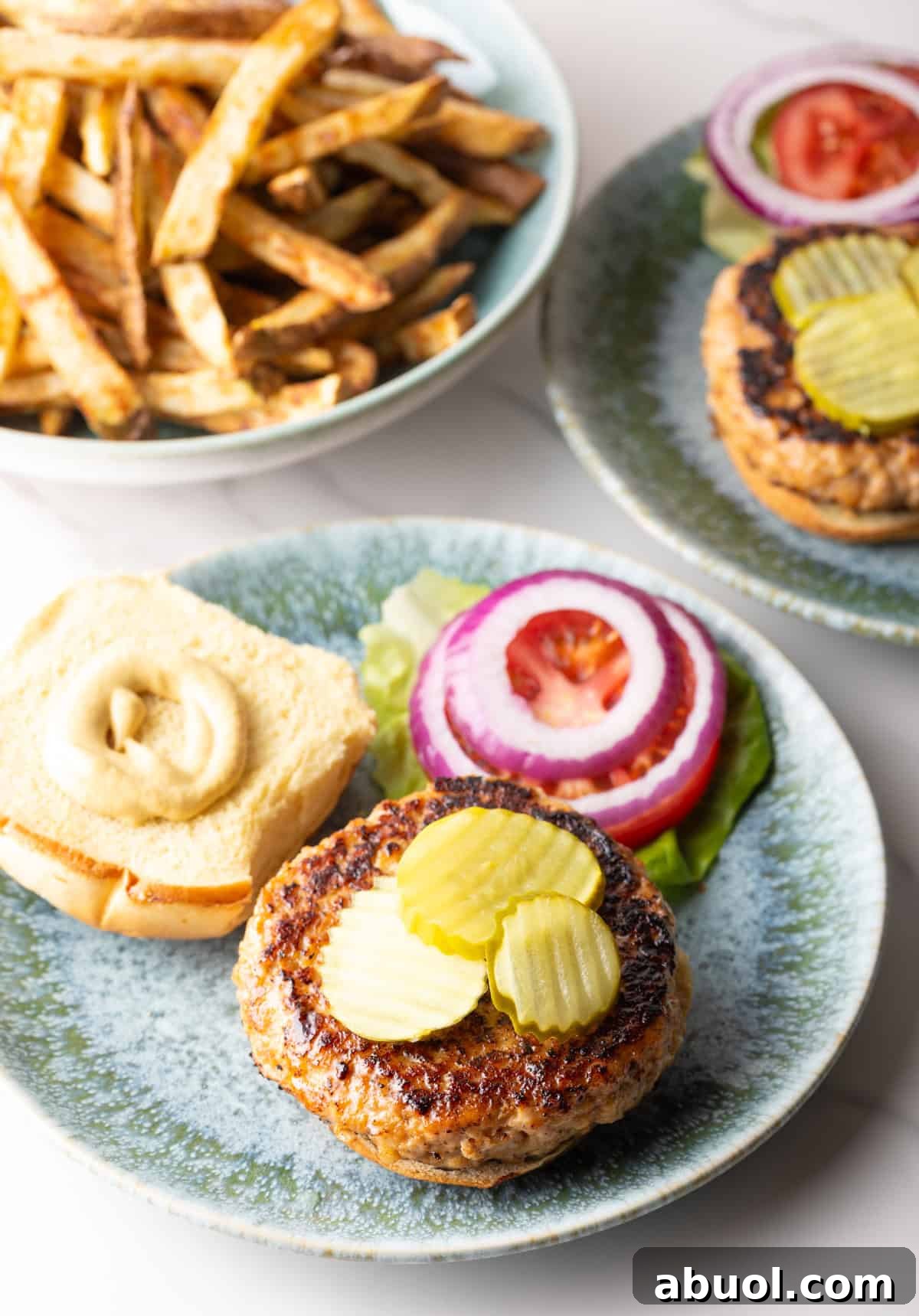 An open chicken patty sandwich topped with pickles, sitting on a plate with vegetable toppings.