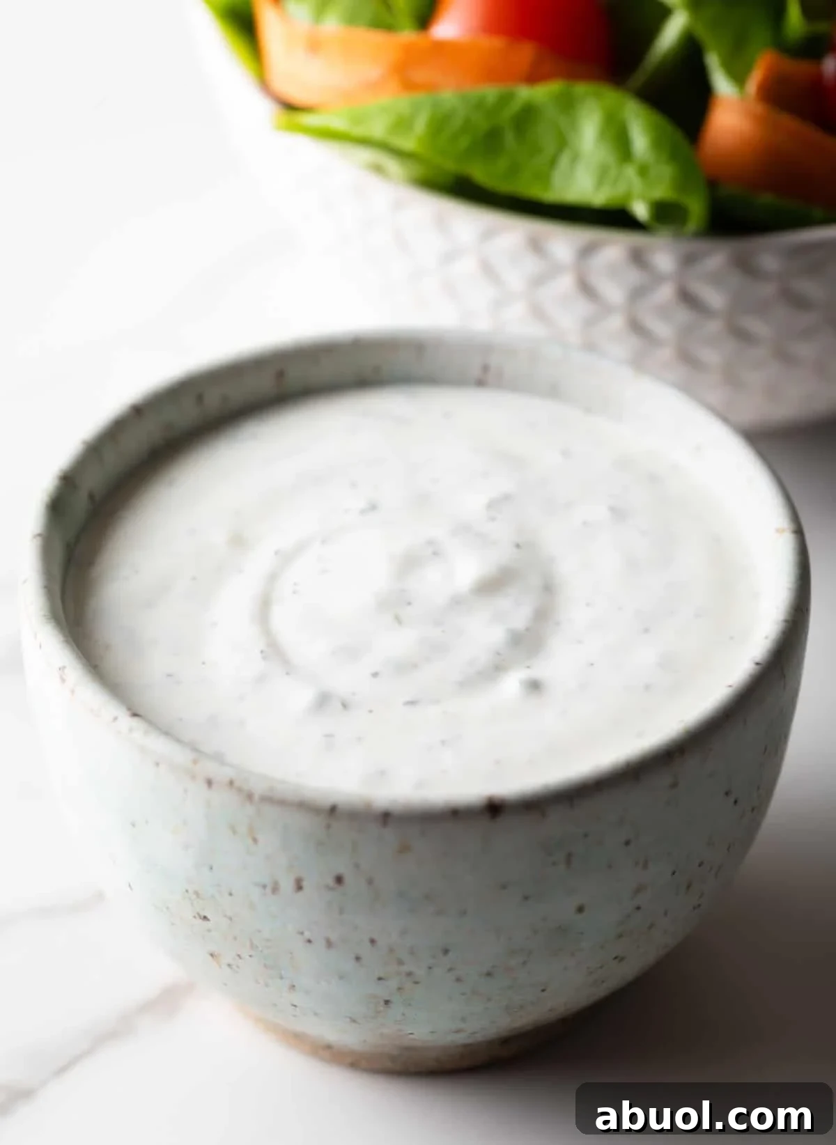 A homemade buttermilk ranch dressing recipe in a white bowl, sitting next to a fresh greens salad.