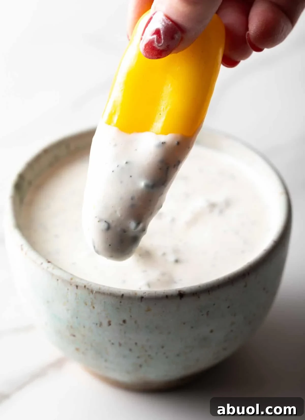 A yellow pepper is being dipped into a bowl filled with homemade ranch dressing made with buttermilk.