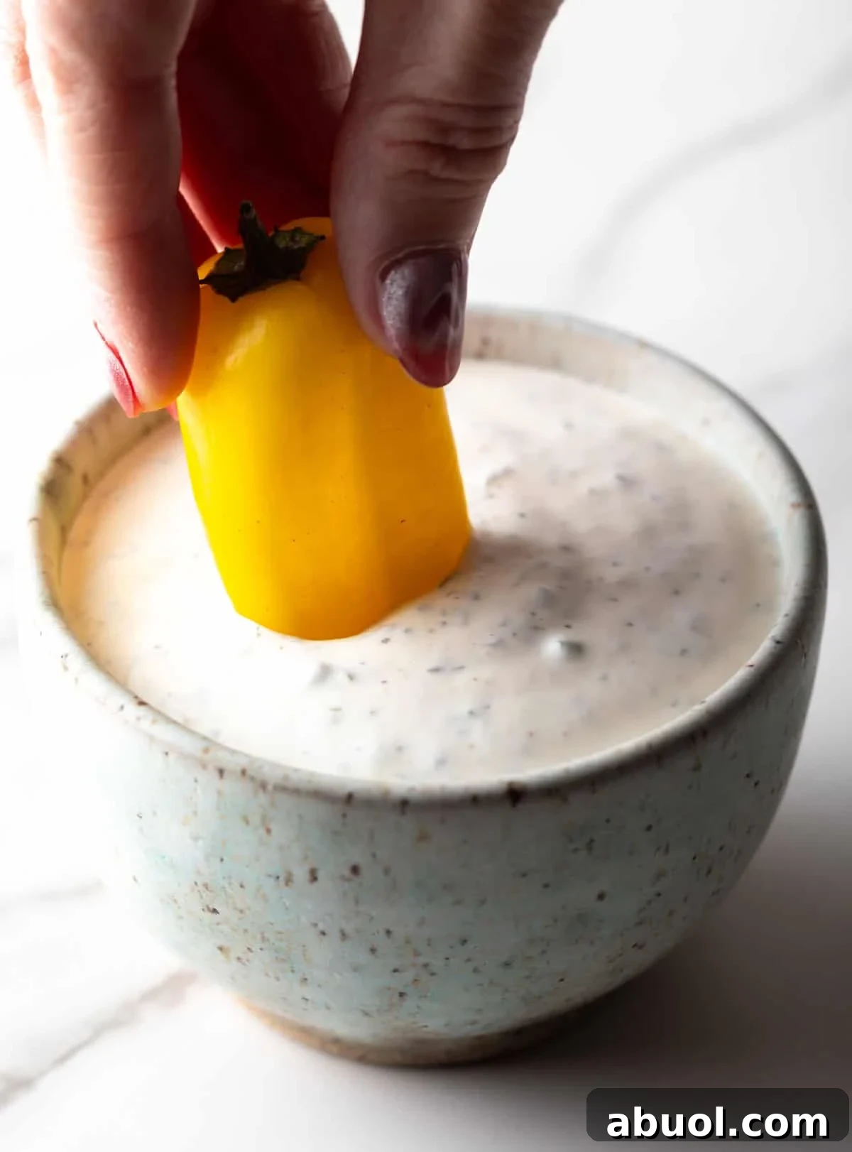 A yellow pepper is being dipped into a bowl filled with a homemade buttermilk ranch dressing recipe.