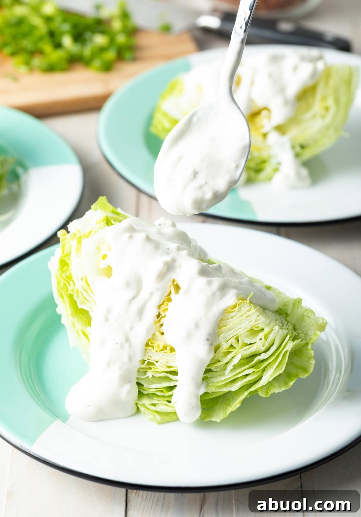 Spoon drizzling blue cheese dressing over a wedge of iceberg lettuce.