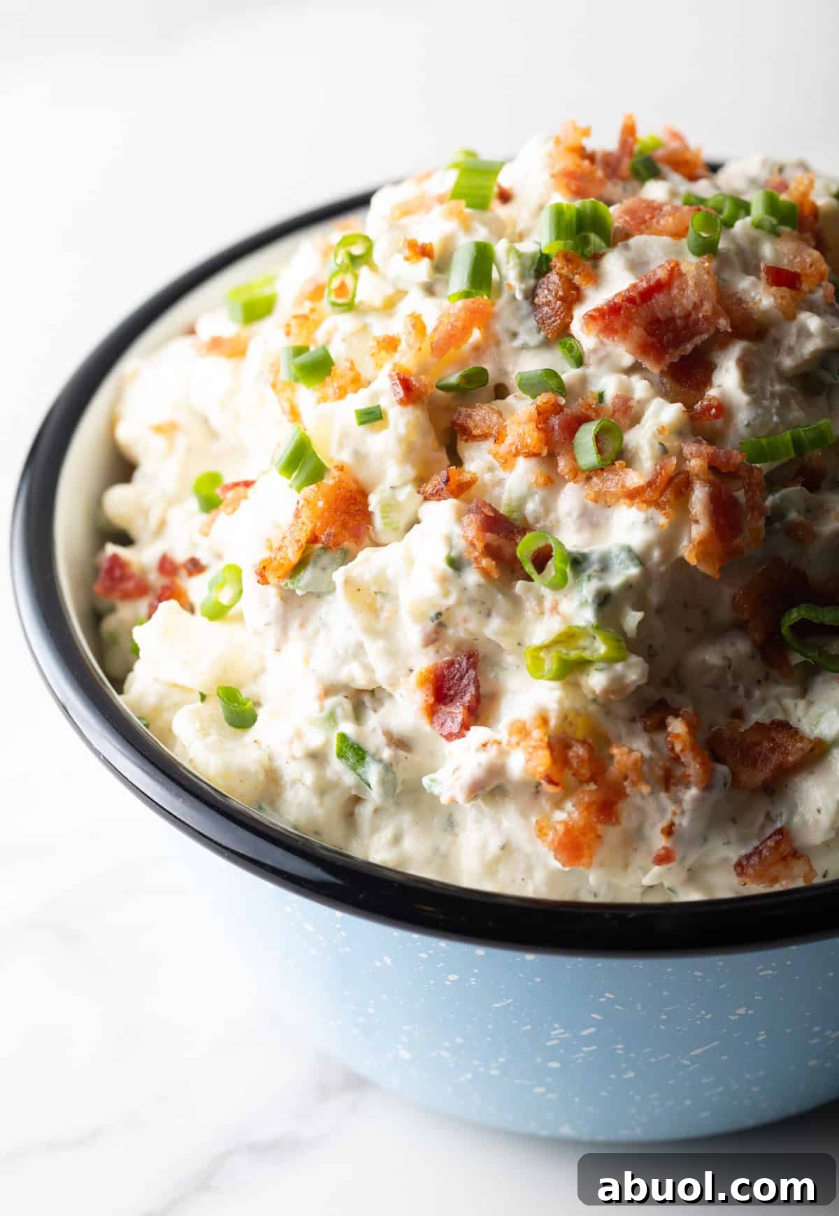 A blue bowl filled with bacon ranch potato salad topped with green onion and chopped bacon.
