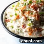 A blue bowl filled with bacon ranch potato salad topped with green onion and chopped bacon.