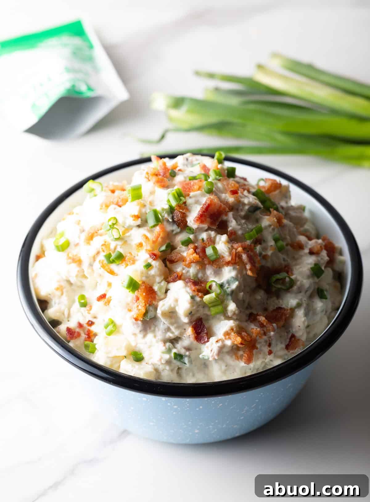 A blue bowl filled with a bacon ranch potato salad recipe in front of a bundle of green onions.