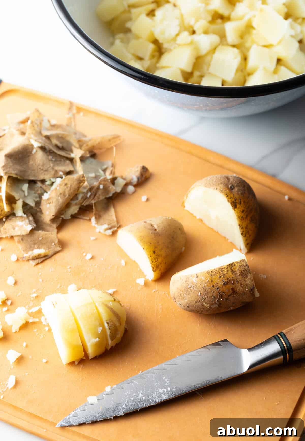 Potatoes are being chopped on a wooden cutting board to prepare for a ranch bacon salad recipe.