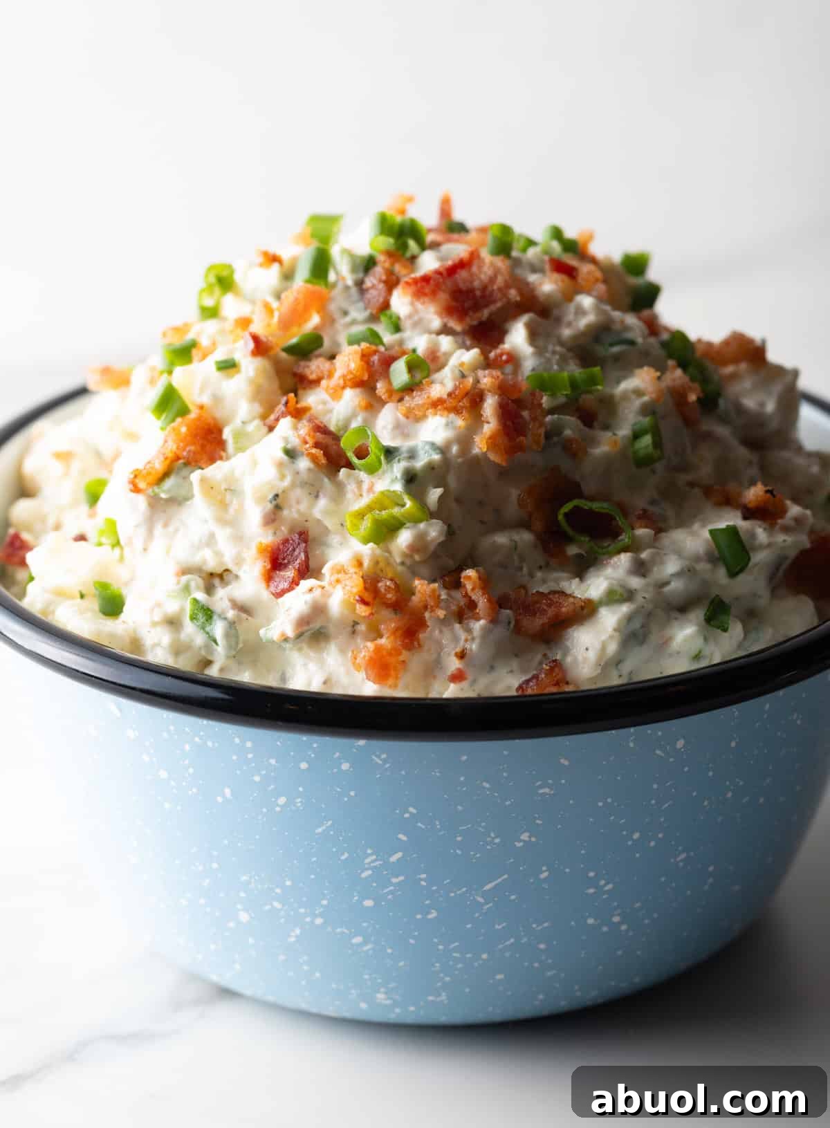 A blue bowl filled with a bacon ranch potato salad recipe topped with green onion and chopped bacon.