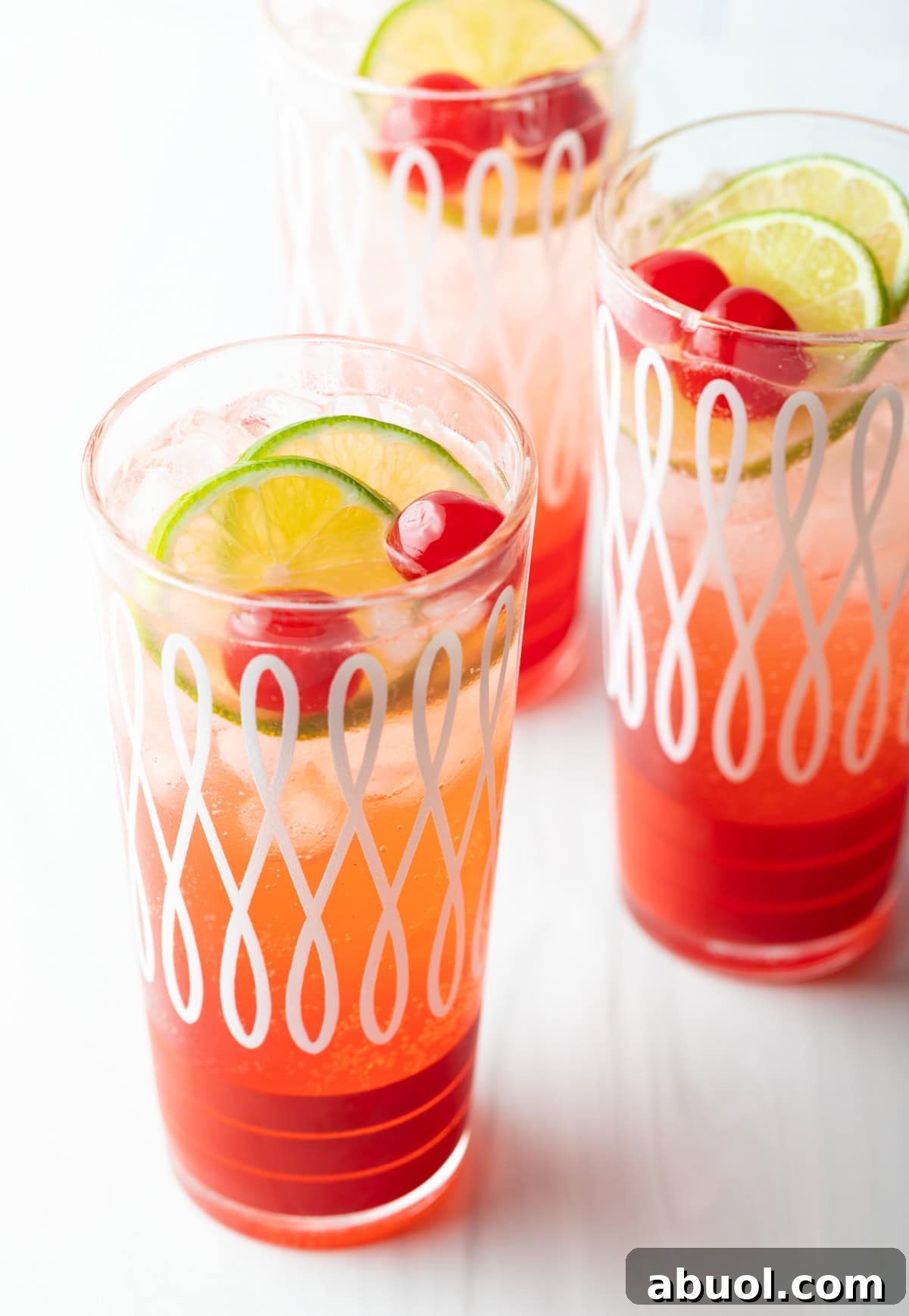 Three glass cups filled with a refreshing cherry limeade recipe, topped with lime wedges and maraschino cherries.