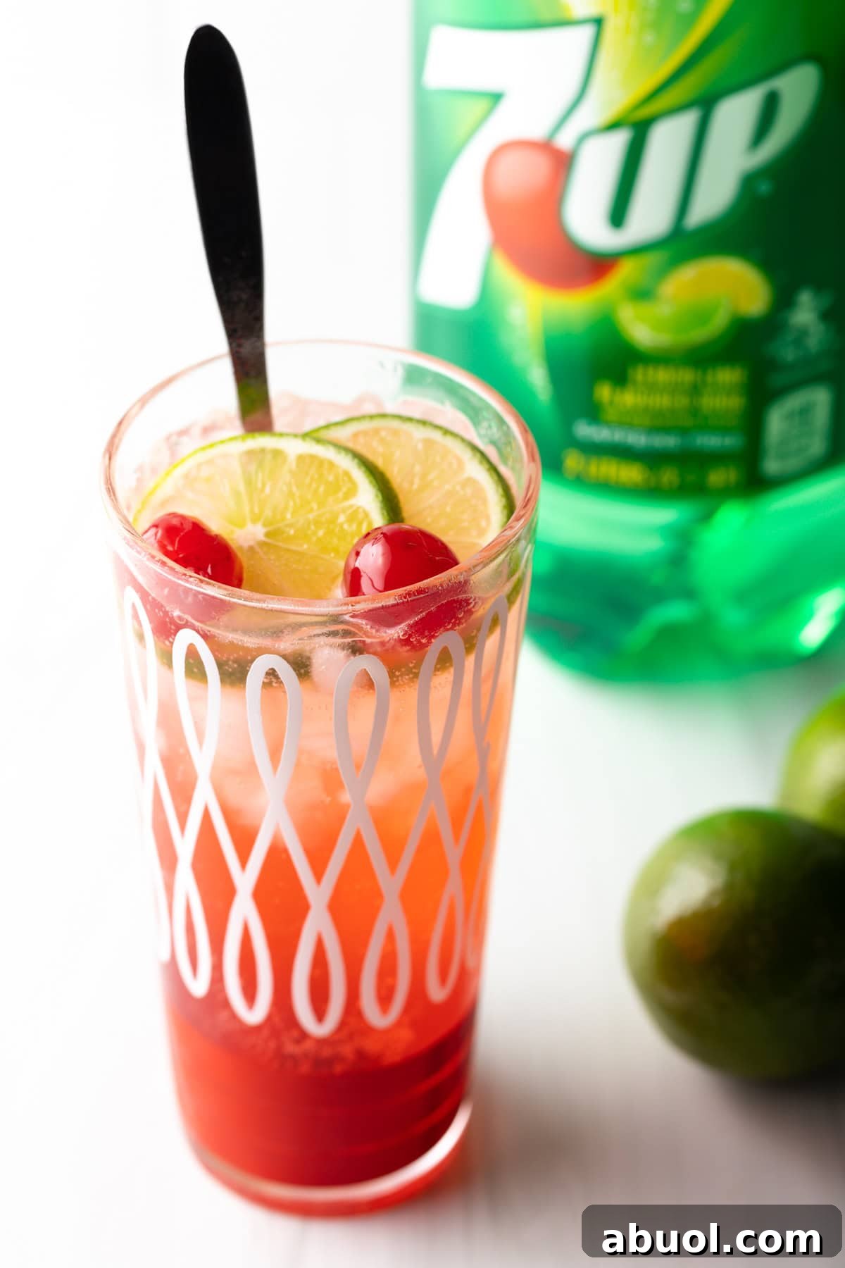 A glass filled with an easy cherry limeade recipe, with a long spoon for stirring.