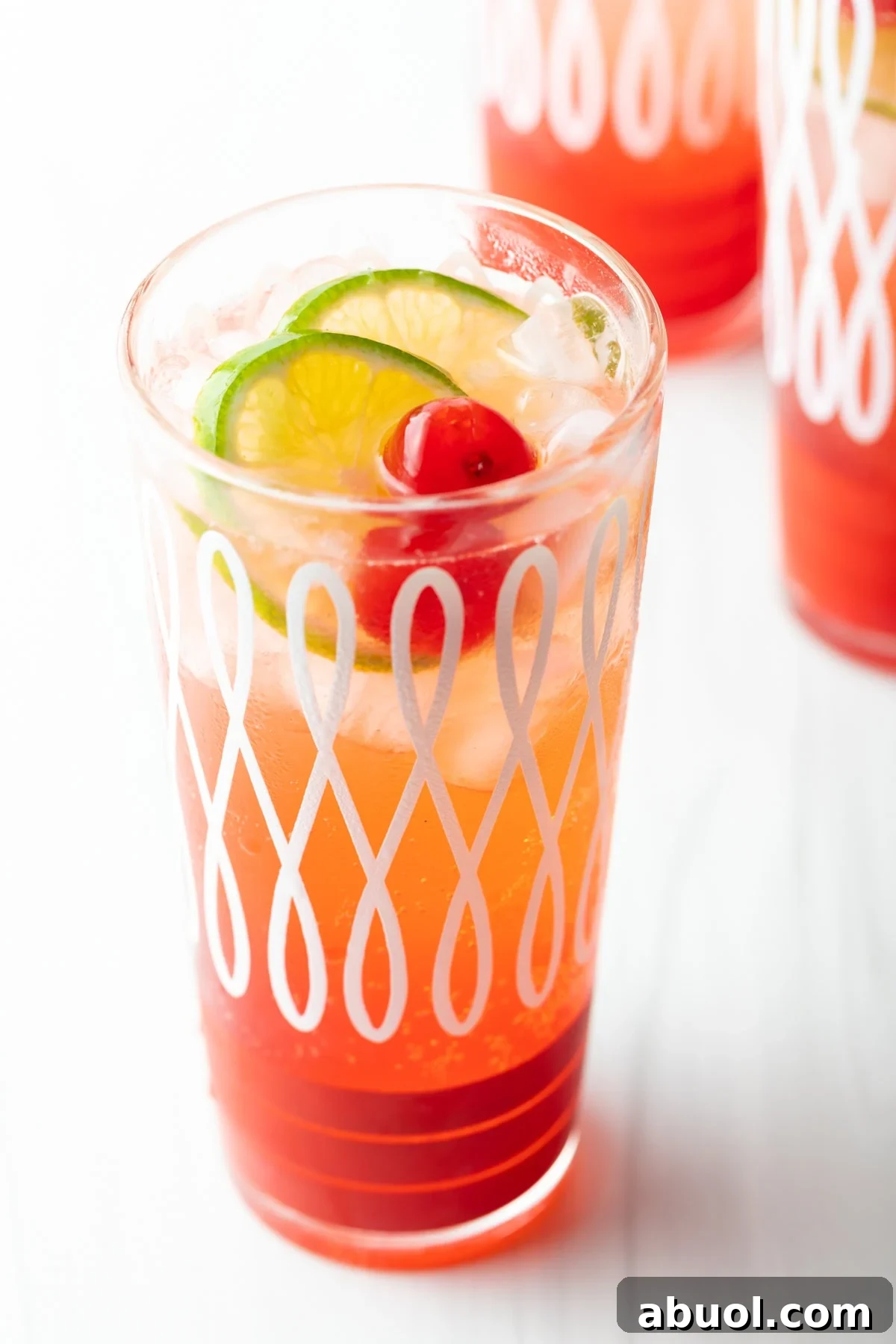 A glass filled with cherry limeade topped with maraschino cherries and lime wedges.