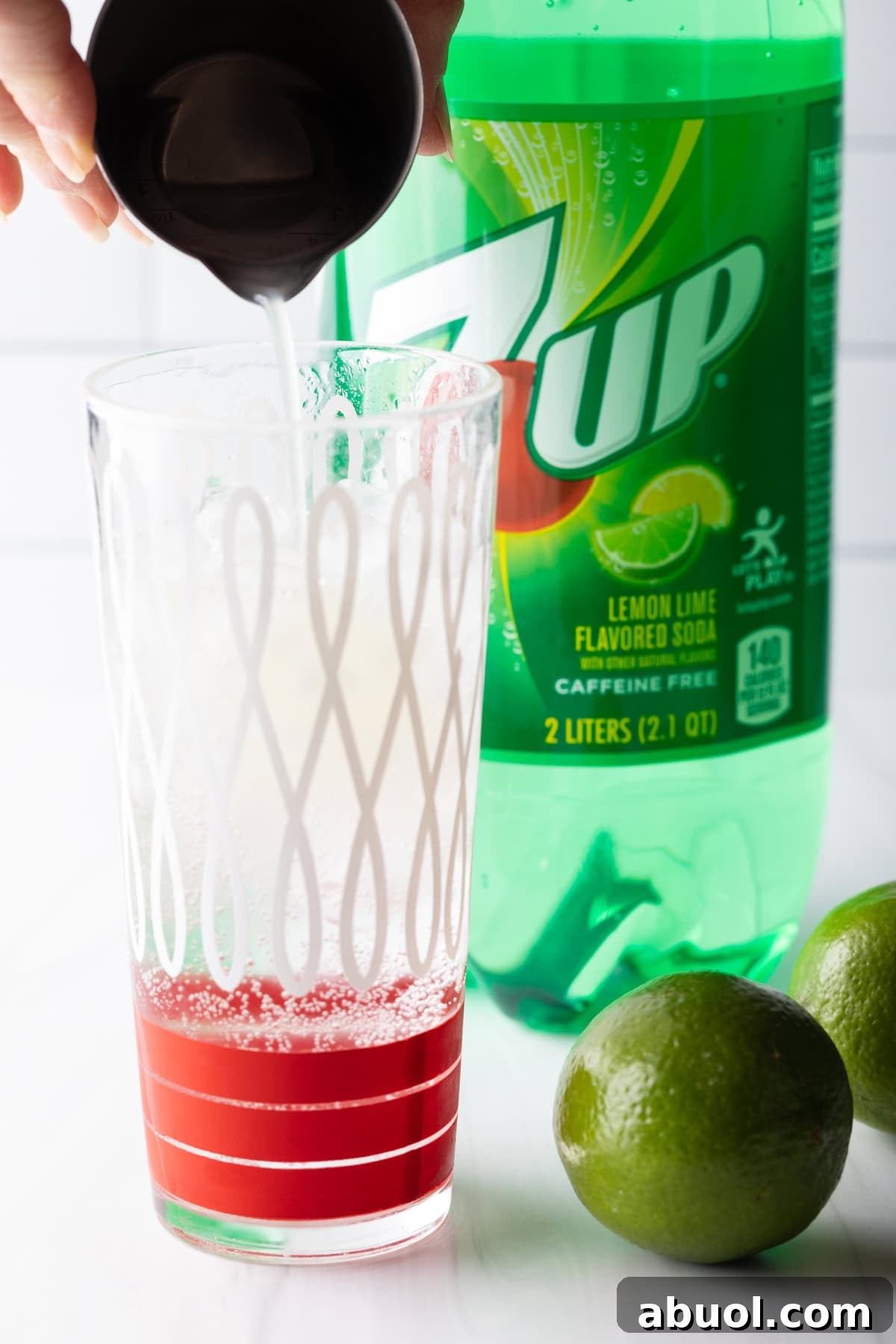 A glass filled with ice with fresh lime juice being poured over the ice.