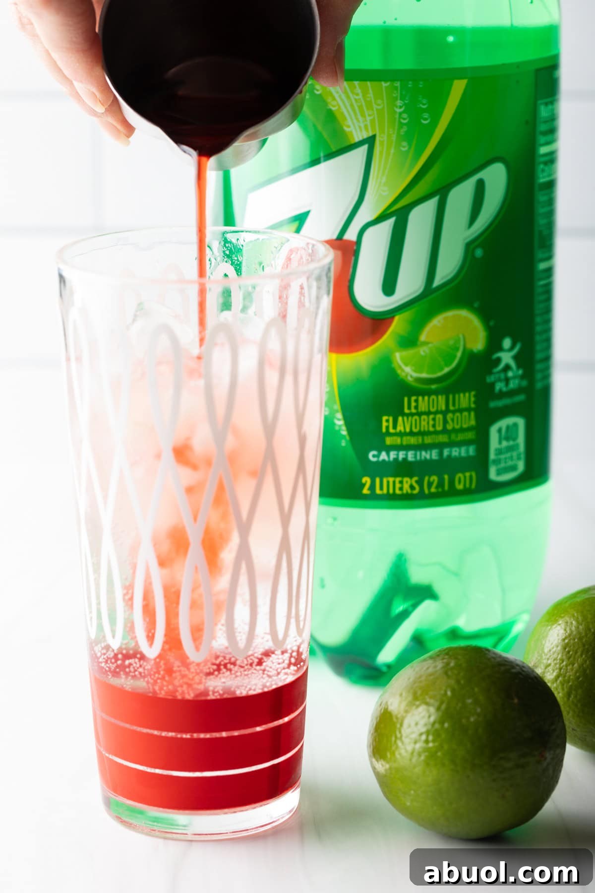 Maraschino cherry juice is being added to a glass filled with ice and lemon-lime soda.
