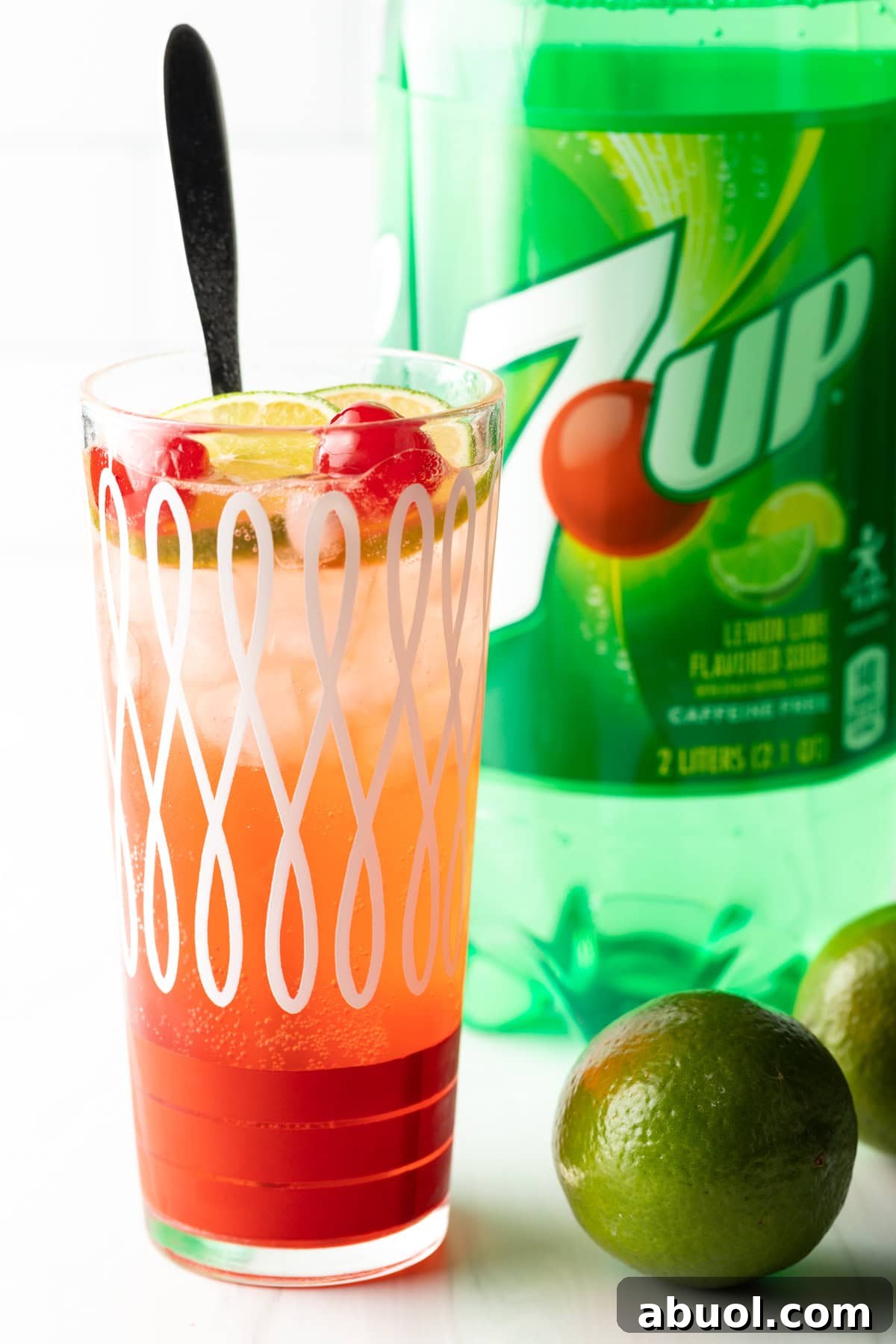 A glass filled with a homemade cherry limeade recipe, with a long spoon for stirring.