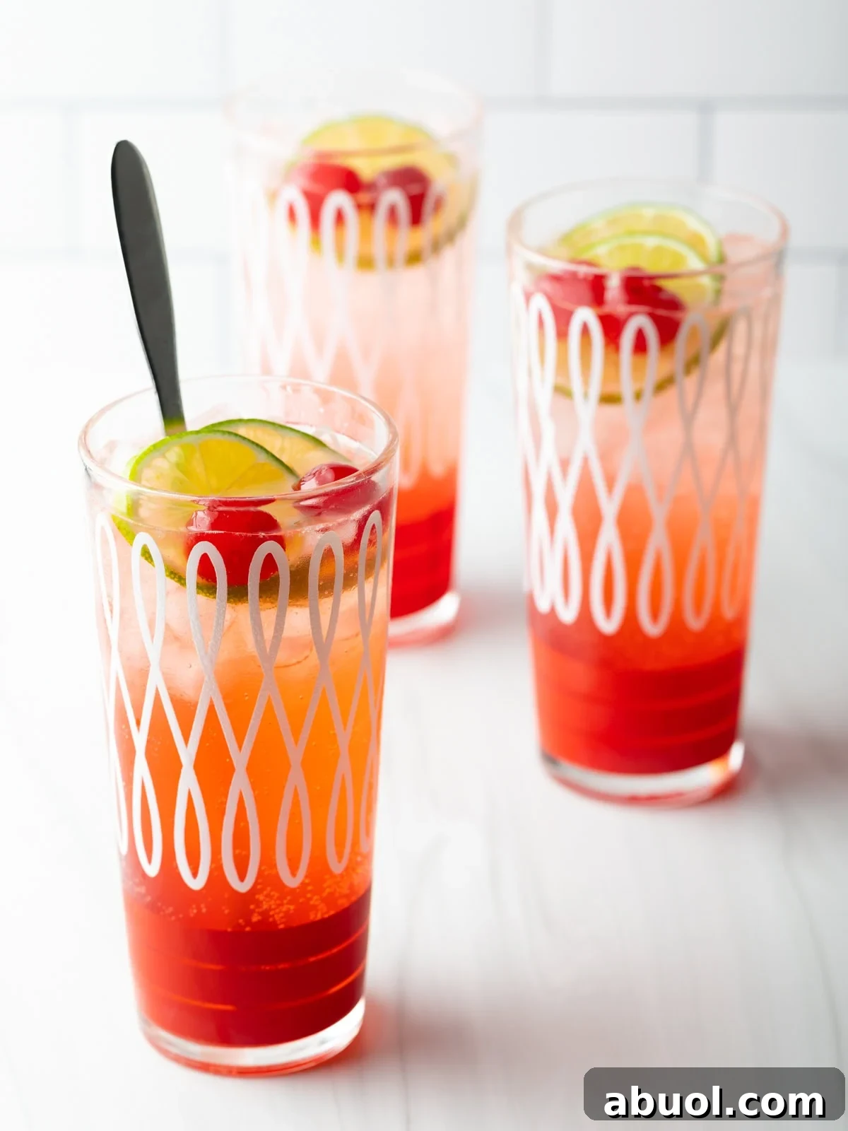 Three glass cups filled with a refreshing cherry limeade recipe, topped with lime wedges and maraschino cherries.