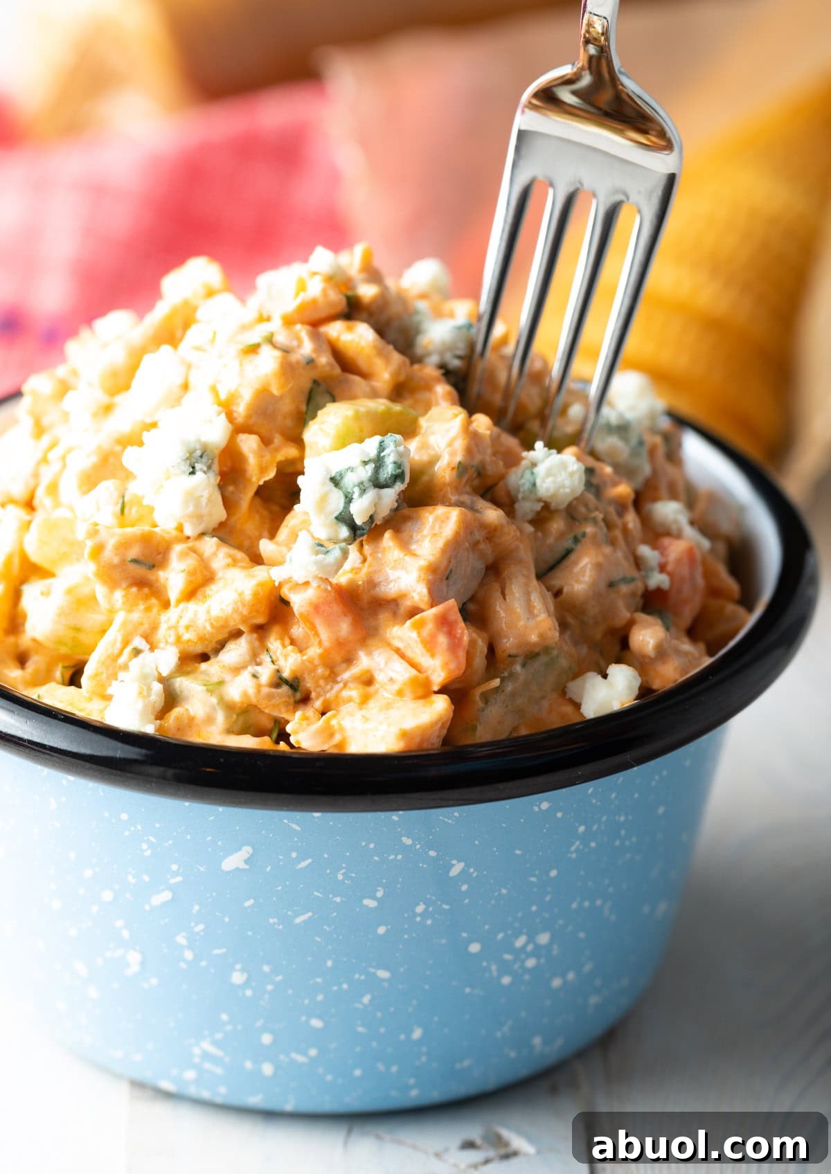 A fork is taking a bite out of buffalo chicken salad in a blue bowl.