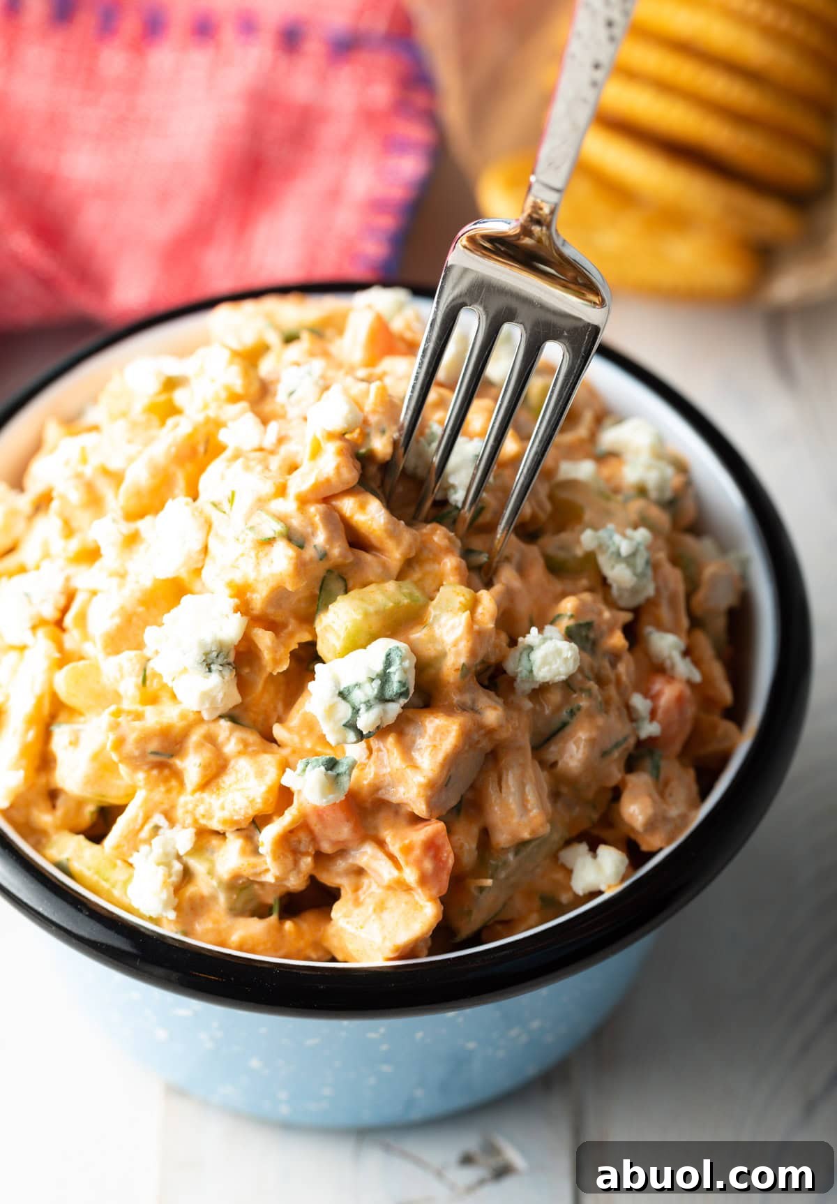 A fork is taking a bite out of buffalo chicken salad in a blue bowl.