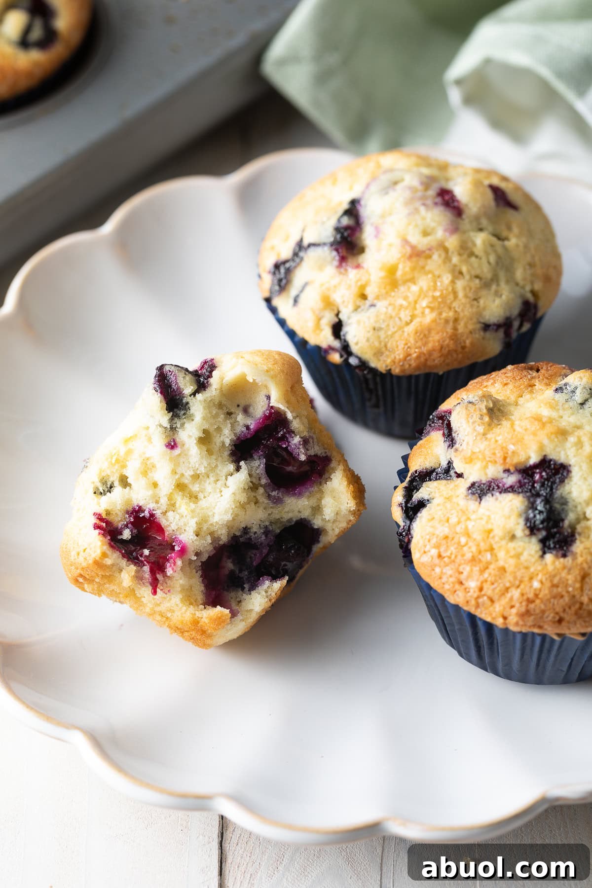 Three blueberry muffins on a white plate, one cut in half.